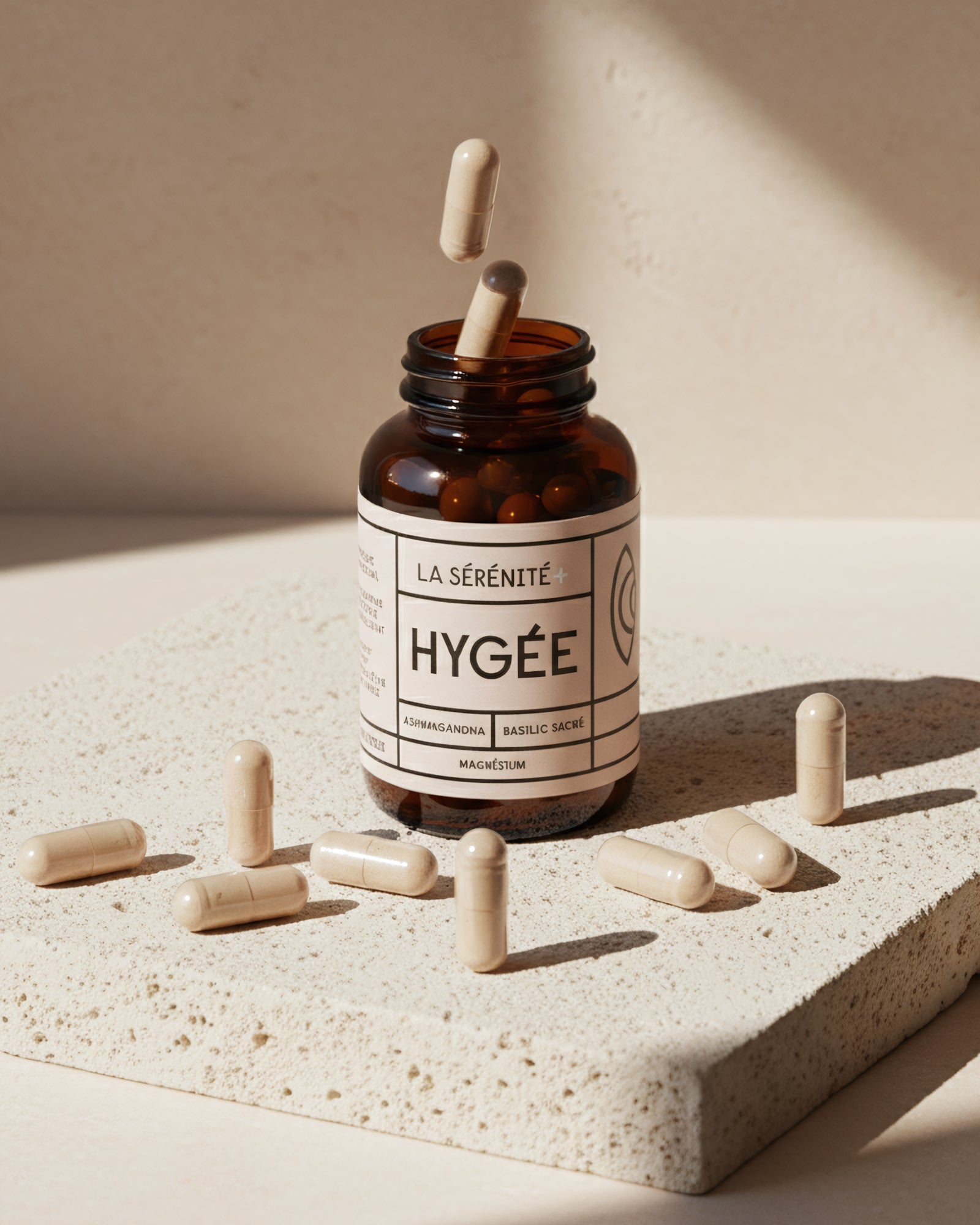 An amber HYGÉE La Sérénité+ bottle sits on a textured stone slab with beige capsules scattered around and two capsules floating above the open neck in bright sun.