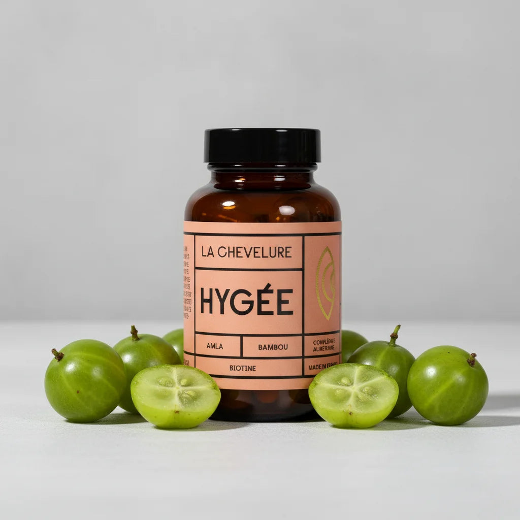 A studio product shot of the Hygée La Chevelure bottle surrounded by fresh green Amla berries, highlighting the key botanical ingredient for hair density and shine.