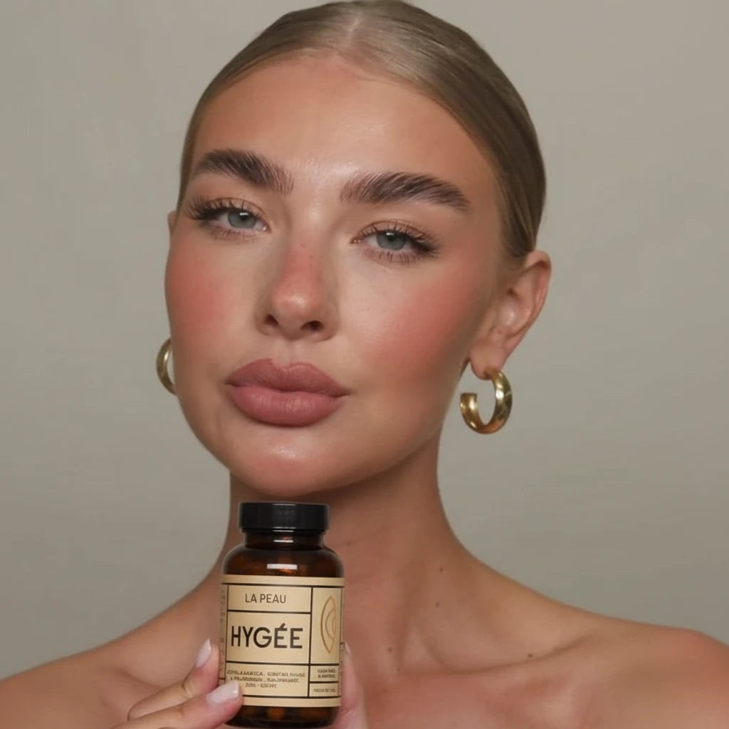 Model with gold hoops displaying HYGÉE La Peau bottle, neutral backdrop, premium French skincare