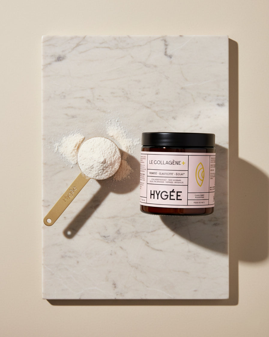 A gold measuring scoop piled with fine white collagen powder sits on a rectangular marble board beside a HYGÉE Le Collagène+ jar, casting long studio shadows on a warm neutral backdrop.