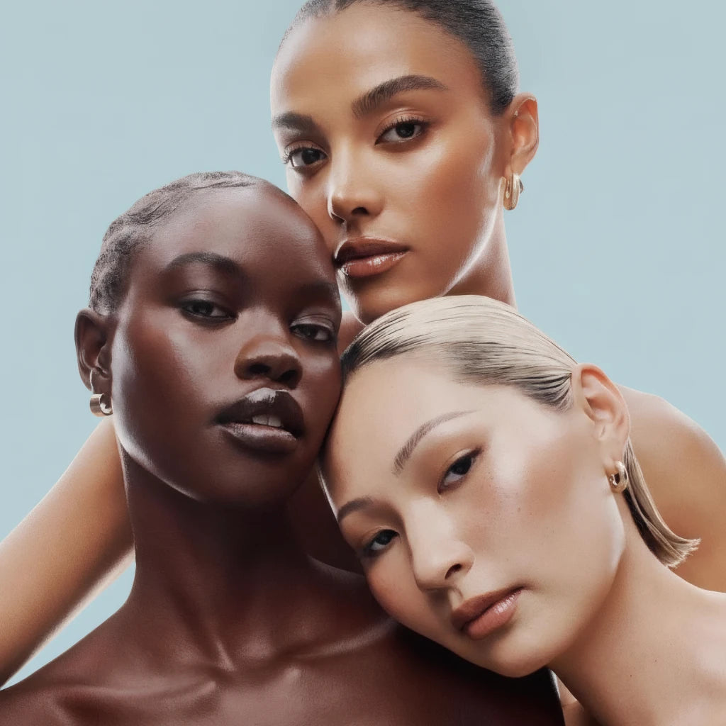 Three models with glowing complexions posing together on soft blue background, beauty results concept for HYGÉE La Résilience