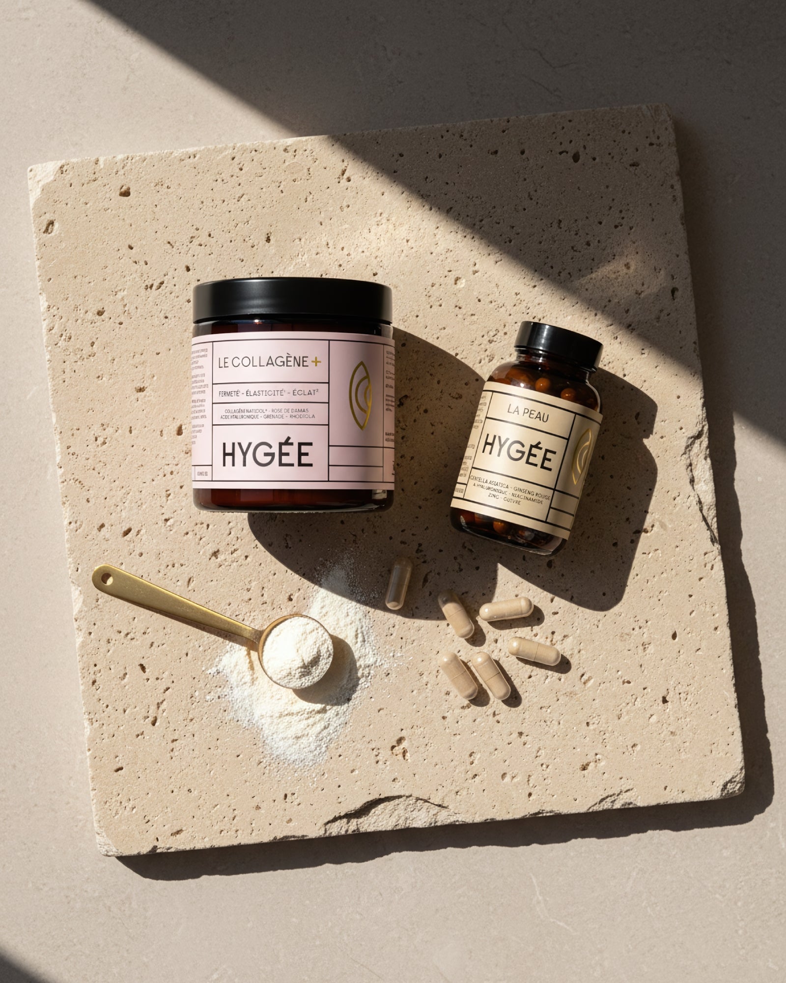 Overhead flatlay showing HYGÉE Le Collagène+ jar and La Peau skin capsules on a textured stone slab with a golden spoon of collagen powder and scattered capsules, illustrating daily dosage and results‑driven inner‑beauty routine.​