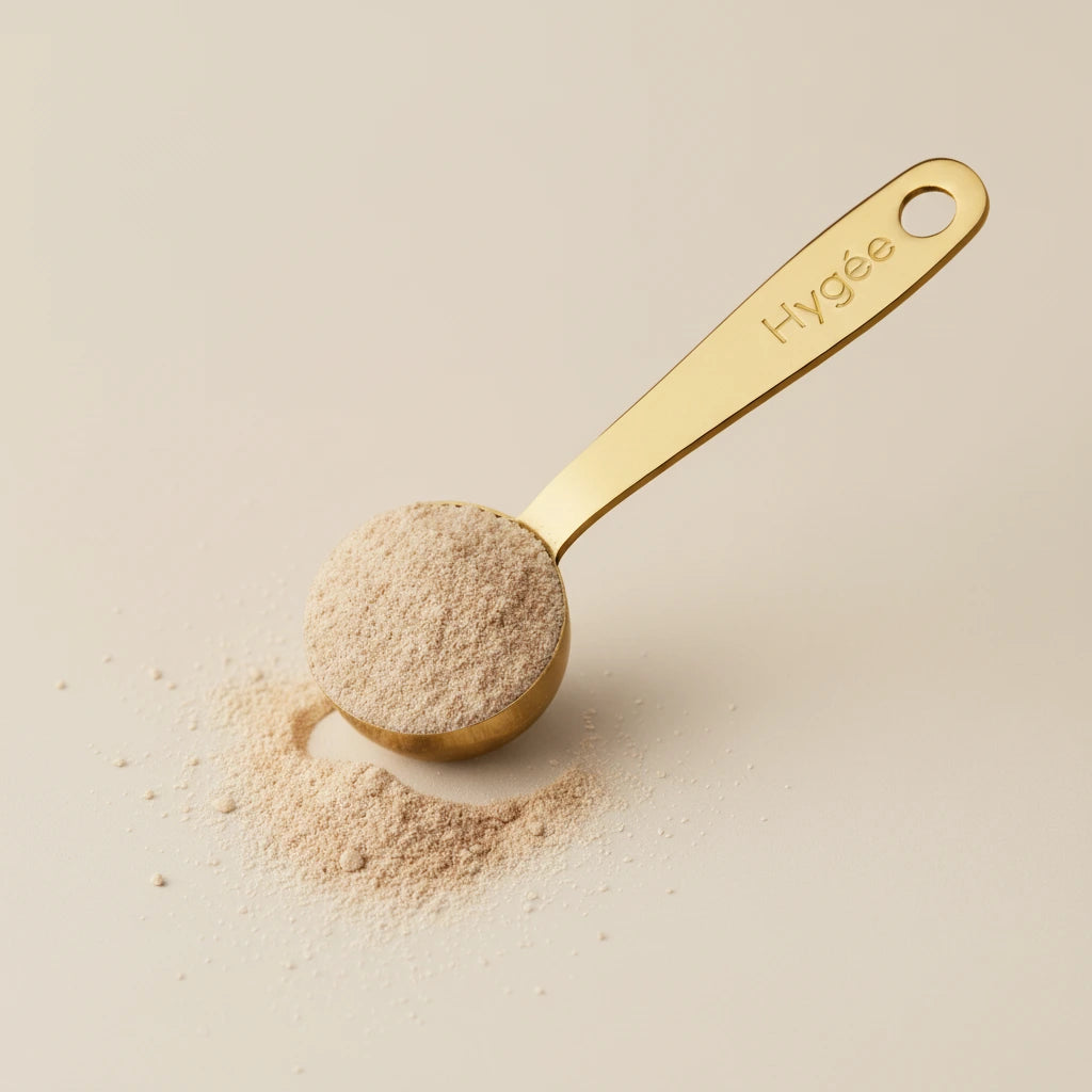 A close-up view of the fine, pinkish HYGÉE Le Collagène+ powder on a golden Hygée-branded measuring spoon.