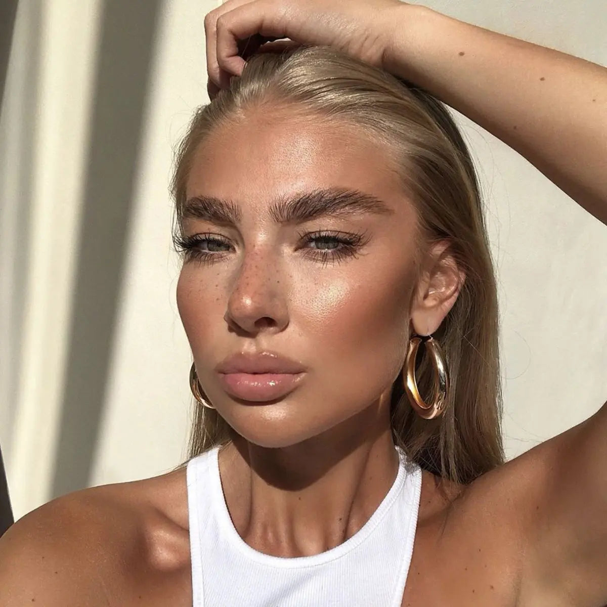Close‑up sunlit portrait with luminous skin, soft freckles, and gold hoops, illustrating refined glow after La Peau ritual